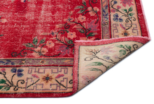 Load image 1 in gallery view. Distressed red rug with floral patterns and a beige geometric border, shown with a corner folded over.