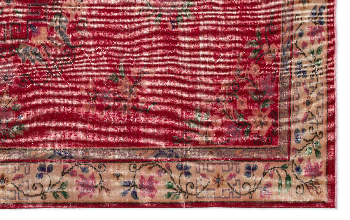 Distressed red rug with a floral pattern and a beige border featuring geometric and botanical motifs.