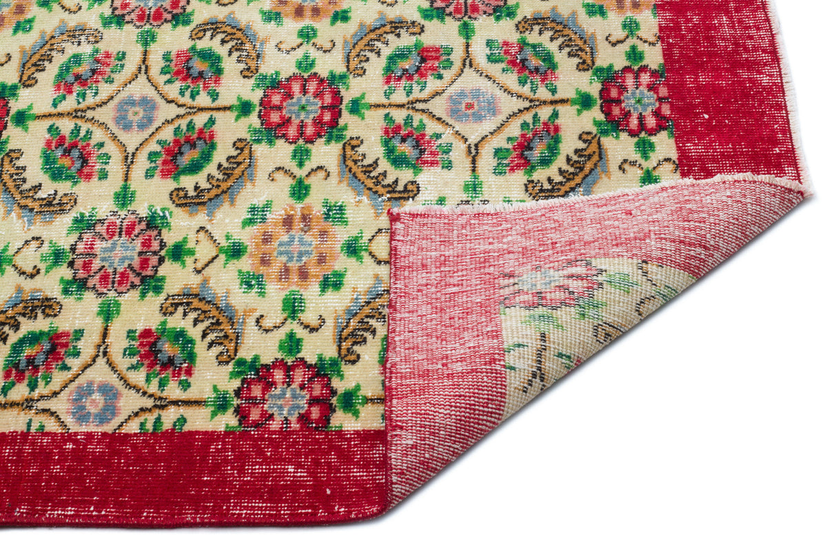 Cream rug with a multi-colored floral medallion pattern and a wide red border, shown with a corner folded over.