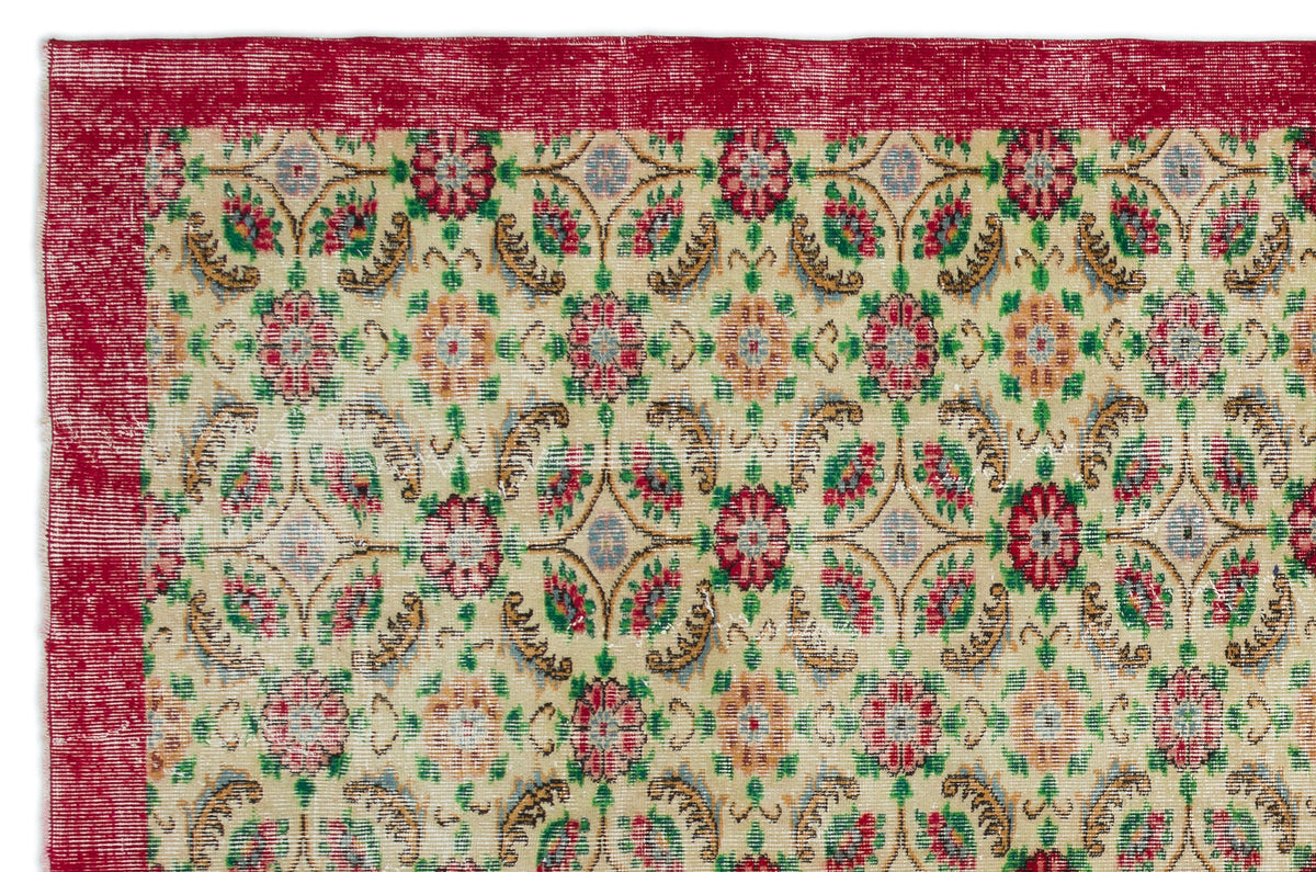 Distressed beige rug with a red border and a repeating floral medallion pattern in red, green, and blue.
