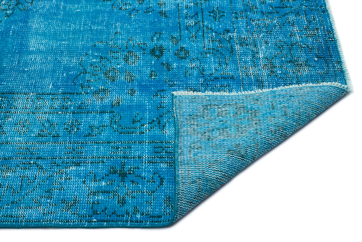 Bright blue distressed rug with a faded traditional medallion pattern and a folded corner showing the woven backing.