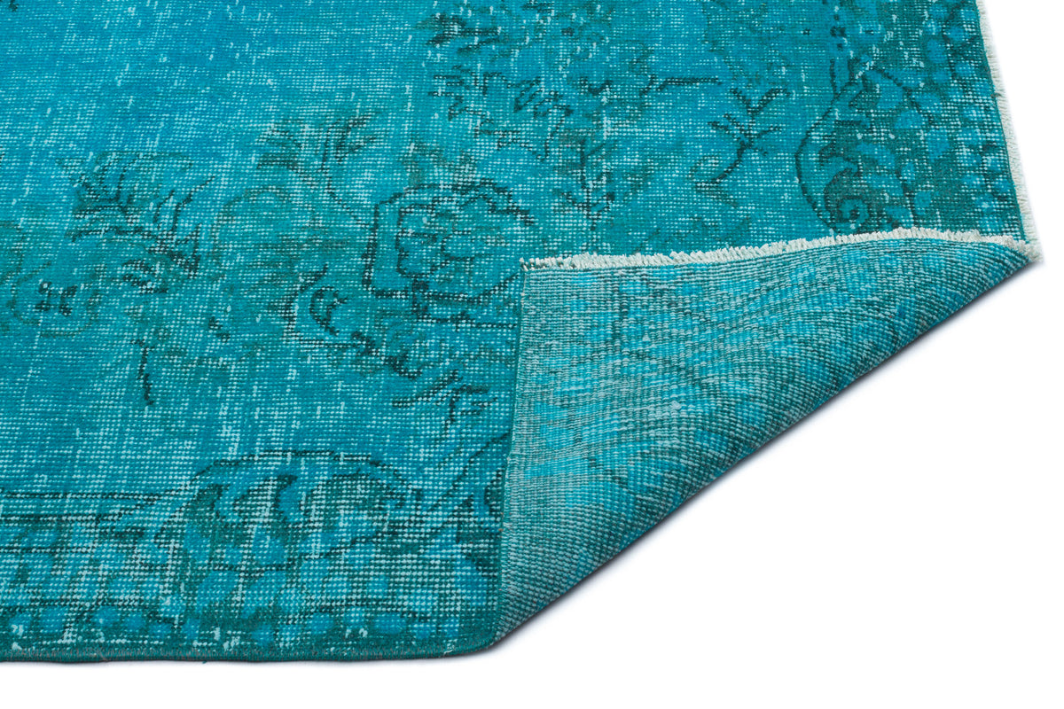 Teal distressed rug with a faded traditional floral pattern and a folded corner showing the woven backing.