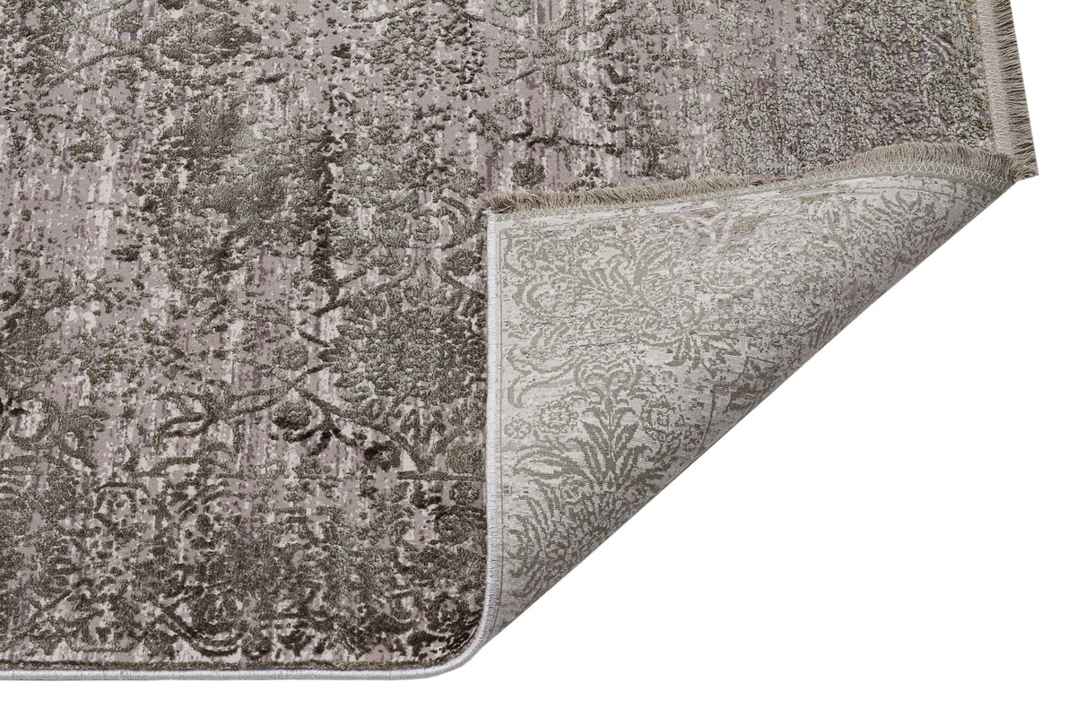Taupe and grey distressed floral rug with a corner folded over to reveal the woven backing.