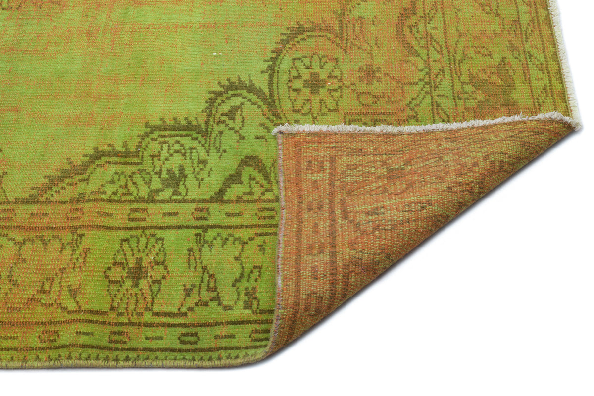 Lime green and brown distressed rug with a traditional floral medallion pattern, shown with a folded corner.