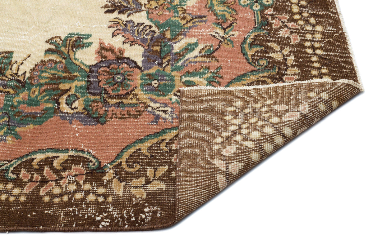 Distressed floral medallion rug in brown, cream, and muted green with a folded corner showing the woven backing.