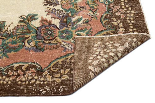 Load image 1 in gallery view. Distressed floral medallion rug in brown, cream, and muted green with a folded corner showing the woven backing.