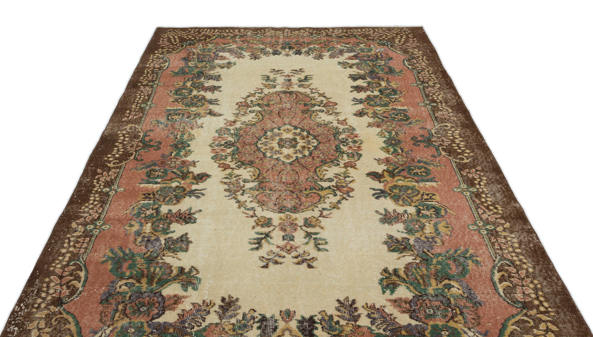 Vintage-style rug with a cream center, floral medallion, and wide brown border featuring muted pink and green accents.