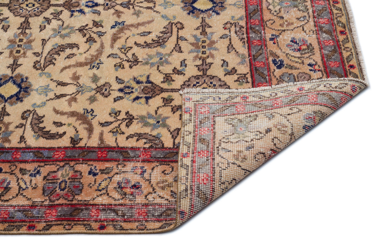 Beige traditional rug with a floral medallion pattern, red and blue accents, and a folded corner showing the backing.