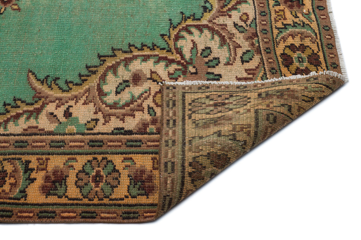 Green and tan traditional rug with a floral medallion border and a folded corner showing the woven backing.