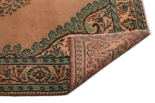 Load image 1 in gallery view. Tan and green traditional rug with a floral medallion border, shown with a corner folded over on a white background.