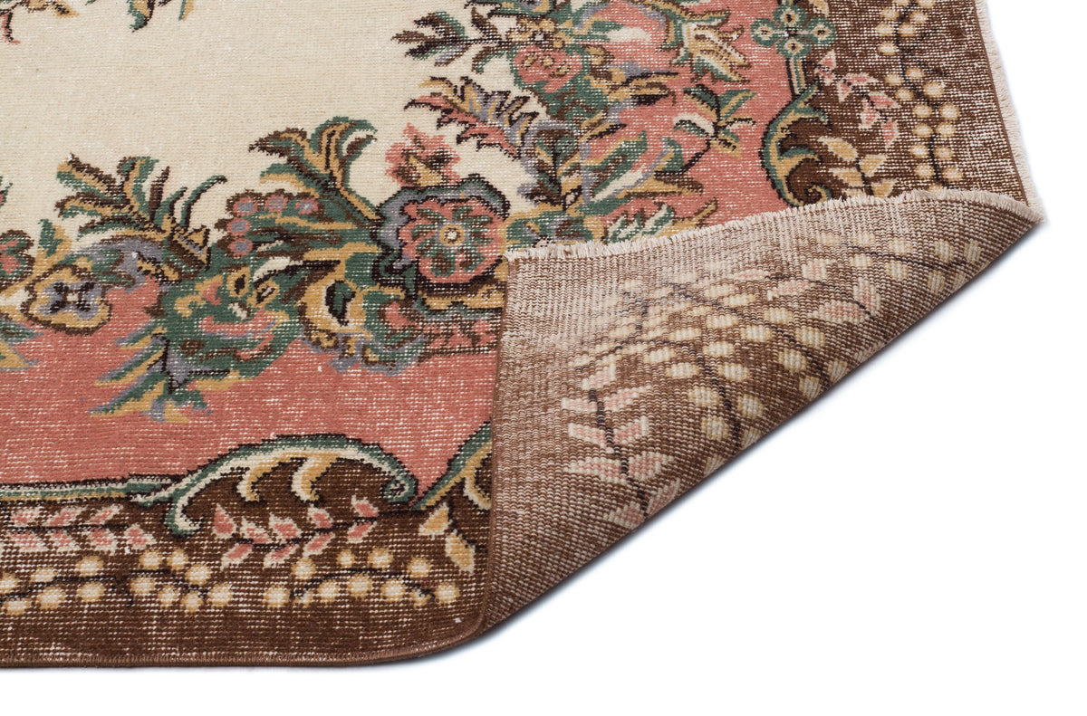 Cream, pink, and brown floral medallion rug with a folded corner showing the woven backing on a white background.
