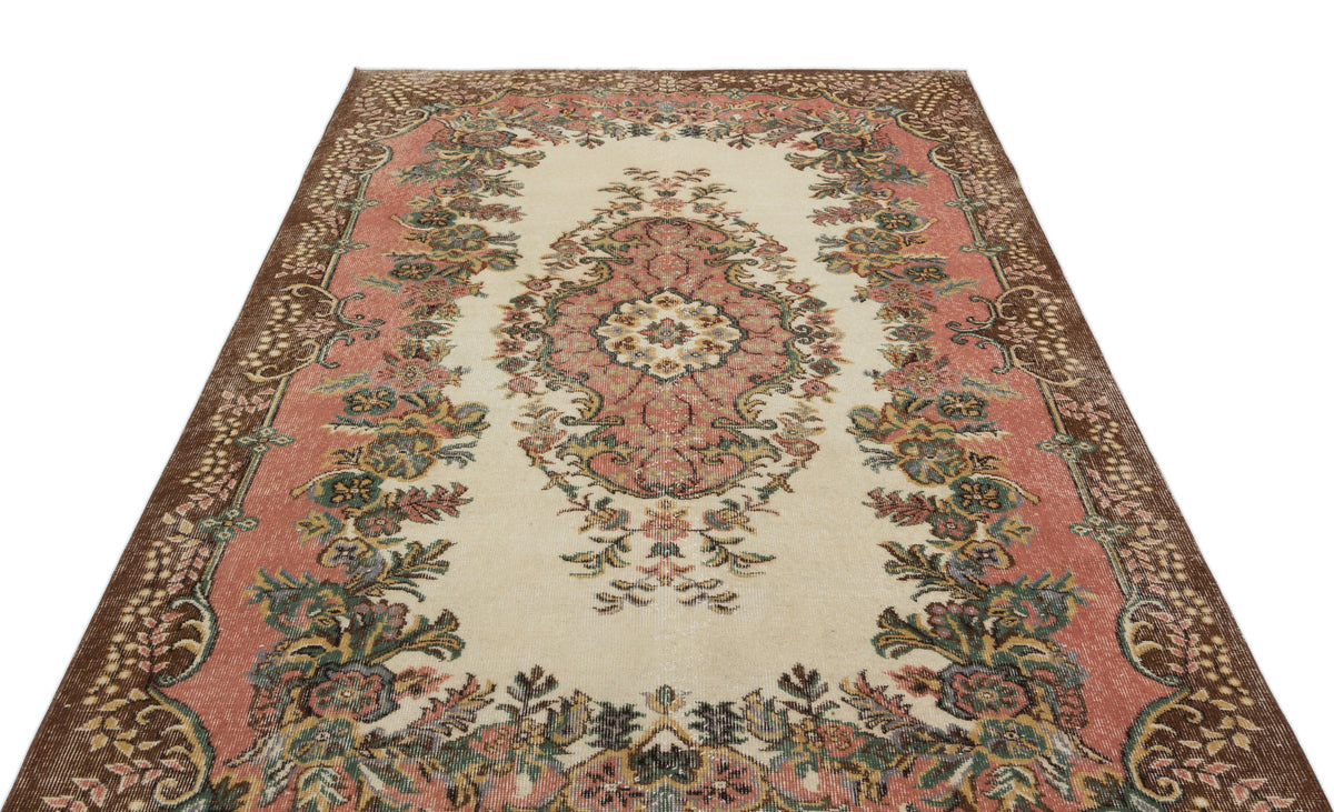 Cream, pink, and brown vintage-style rug with a central floral medallion and ornate border pattern.