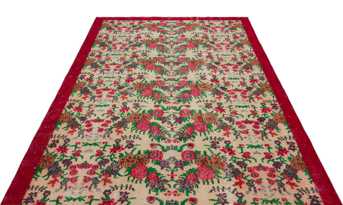 Beige vintage rug with a red border and a repeating floral pattern in pink, green, and purple.