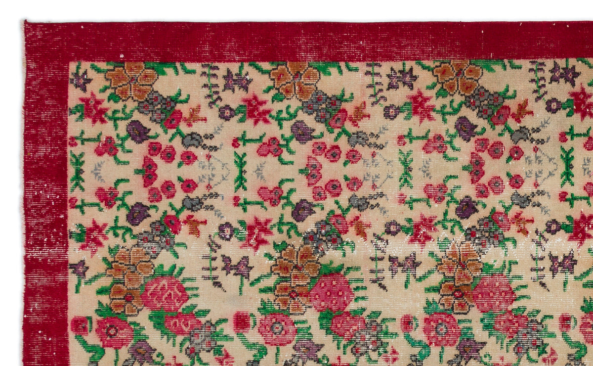 Beige rug with a red border and a repeating floral pattern in red, green, and purple on a white background.