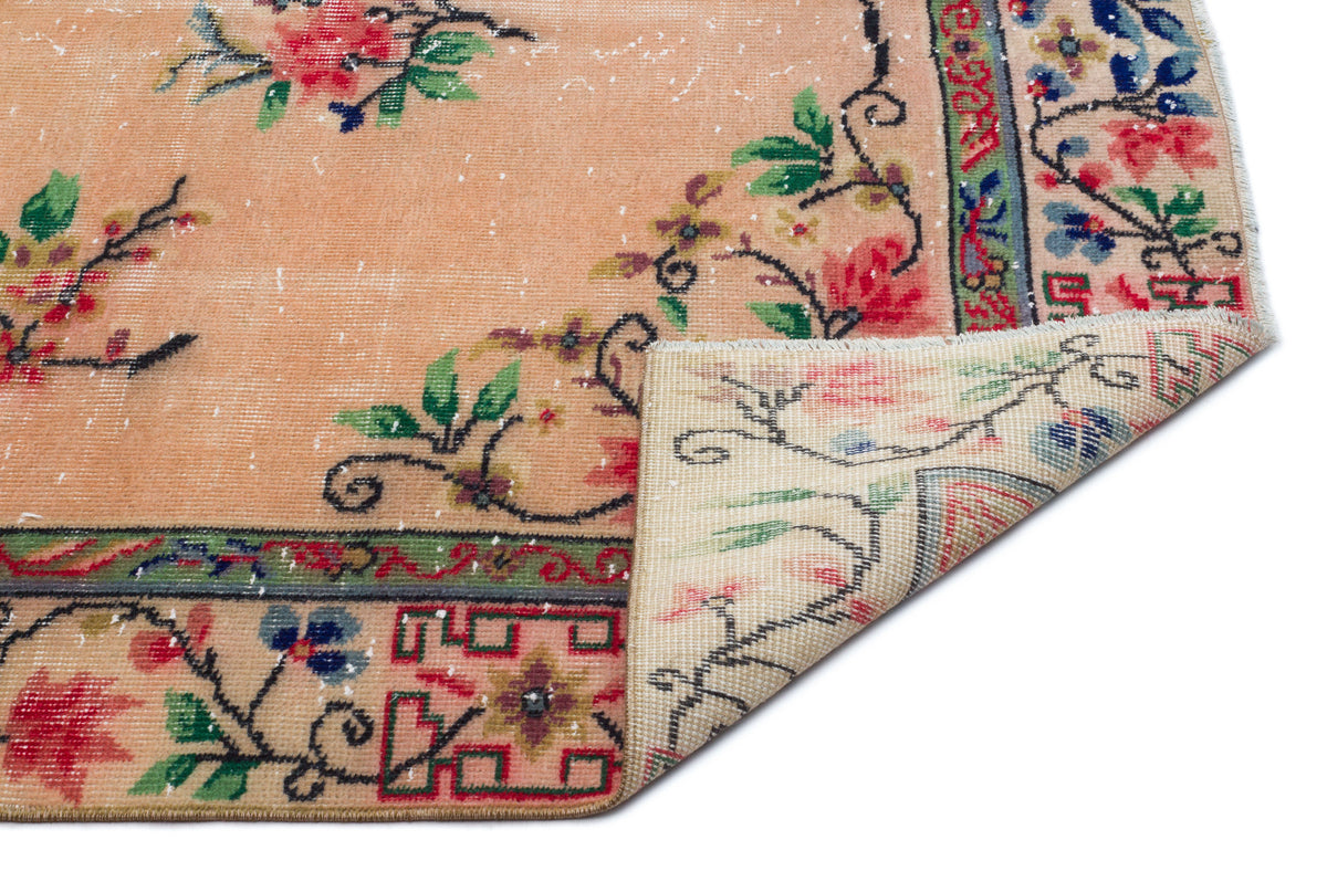 Peach distressed rug with floral motifs, green and red geometric borders, and a folded corner on a white background.