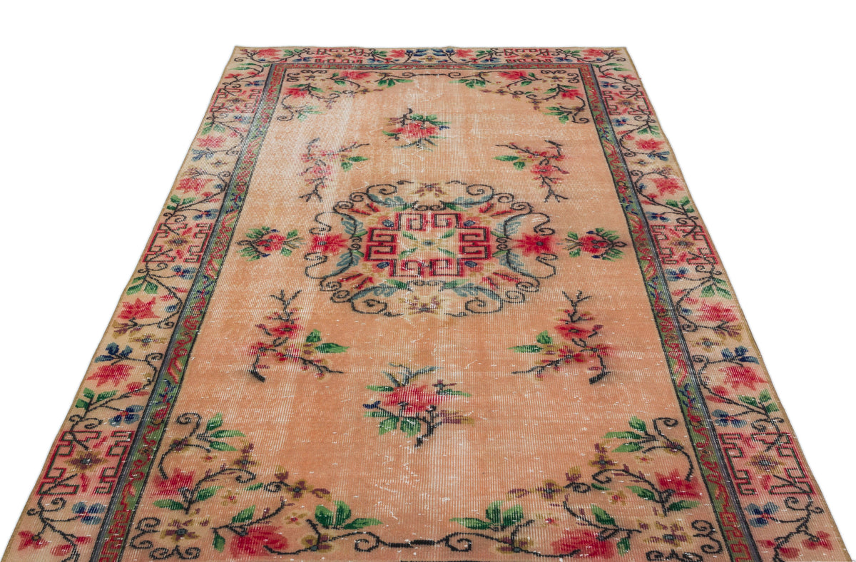 Peach vintage-style rug with a central geometric medallion, floral motifs, and a decorative border on a white background.