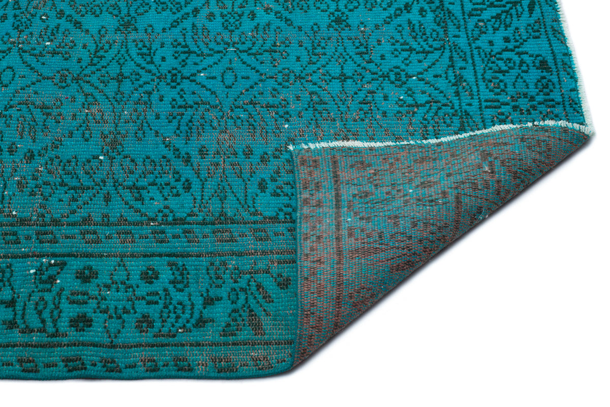 Teal and charcoal rug with a traditional floral medallion pattern, shown with a corner folded to reveal the backing.