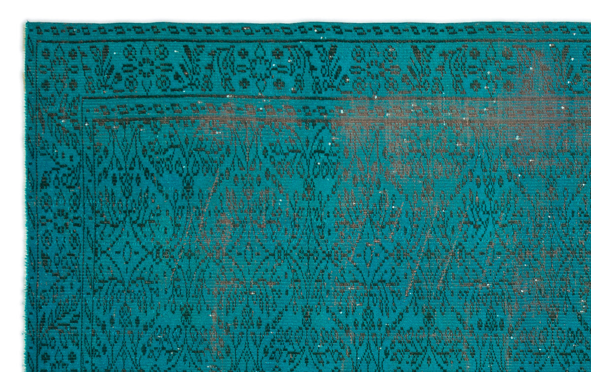 Teal rug with a dark charcoal floral and geometric pattern, featuring a distressed, overdyed finish.