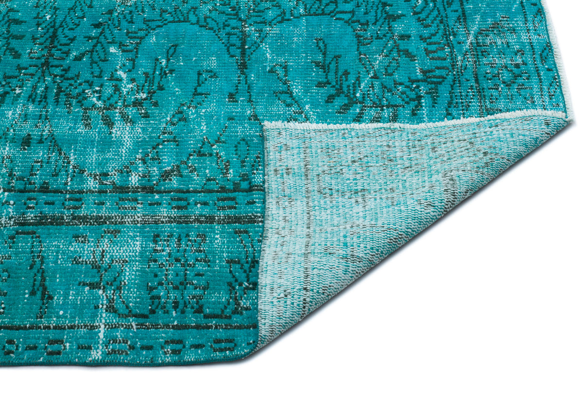 Teal distressed rug with a dark floral medallion pattern, showing a folded corner revealing the lighter underside.
