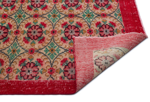 Load image 1 in gallery view. Tan rug with a red floral lattice pattern and a wide red border, shown with a corner folded over on a white background.