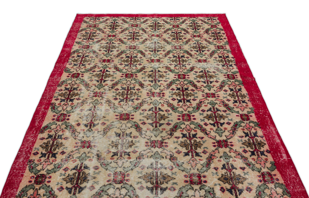Beige vintage rug with a red border and a repeating floral medallion pattern in red, green, and dark blue.