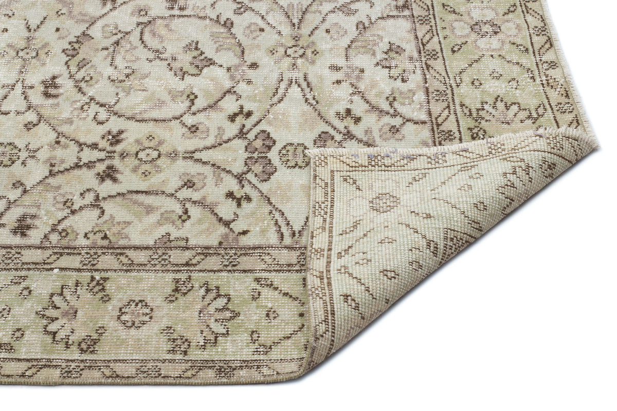 Beige and sage green vintage-style rug with a floral medallion pattern and a folded corner showing the woven backing.