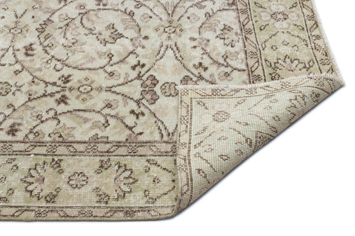 Load image 1 in gallery view. Beige and sage green vintage-style rug with a floral medallion pattern and a folded corner showing the woven backing.