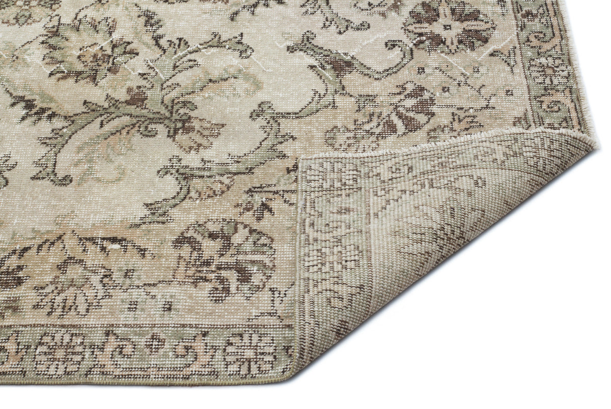 Beige and sage green vintage-style rug with a distressed floral pattern and a folded corner showing the woven backing.