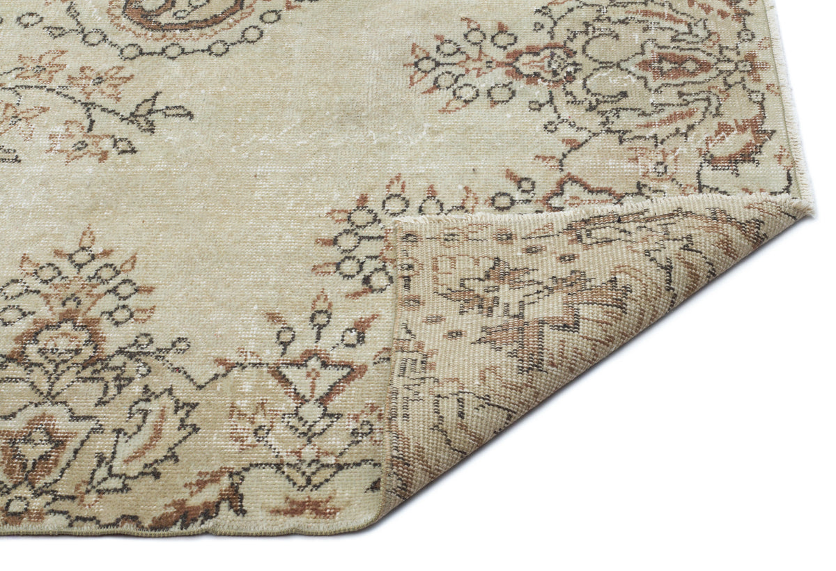 Beige rug with a distressed floral medallion pattern in brown and charcoal, shown with a folded corner on white.