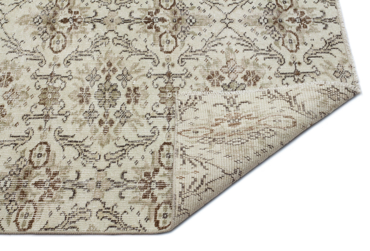 Beige and brown traditional floral medallion rug with a distressed finish, shown with a corner folded over.