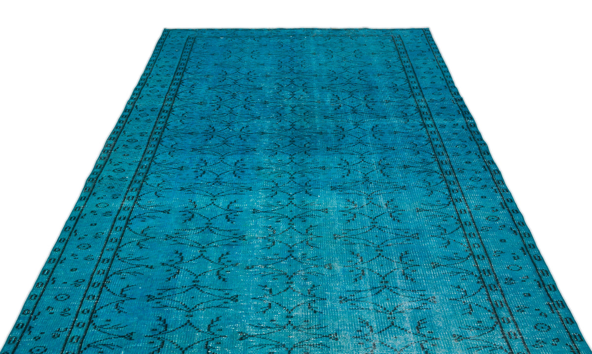 Bright turquoise rug with a distressed black geometric floral pattern and a bordered edge on a white background.