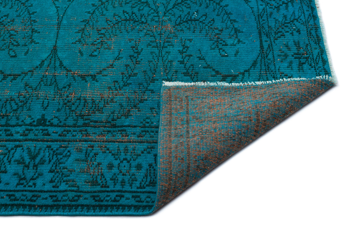 Teal rug with a dark floral medallion pattern and a folded corner revealing a brown underside.