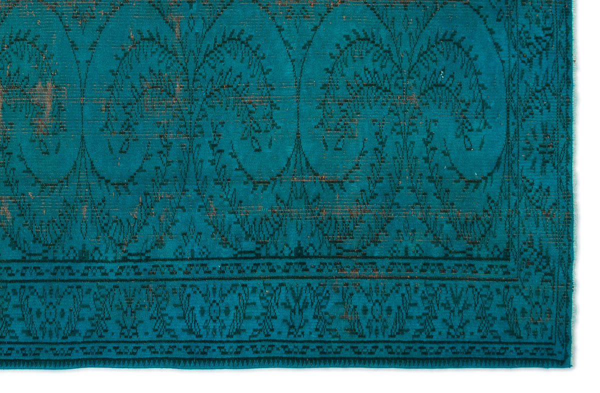 Teal rug with a distressed black botanical medallion pattern and a geometric border.