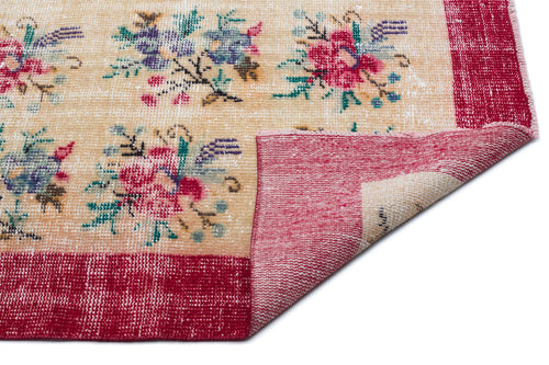 Load image 1 in gallery view. Beige rug with a distressed floral pattern in red, blue, and green, featuring a wide red border and a folded corner.