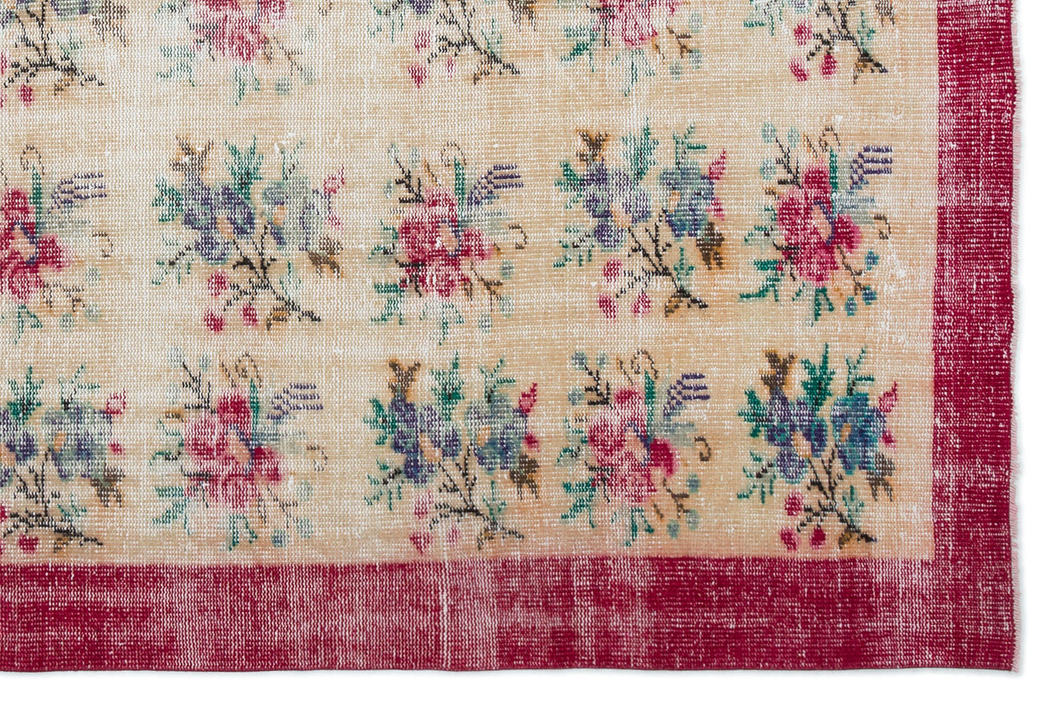 Beige rug with a repeating floral bouquet pattern in pink, blue, and green, framed by a distressed red border.
