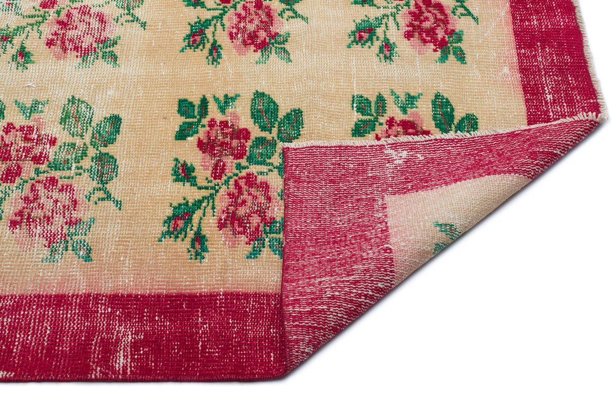 Beige rug with a red floral pattern and border, featuring a folded corner revealing the underside.