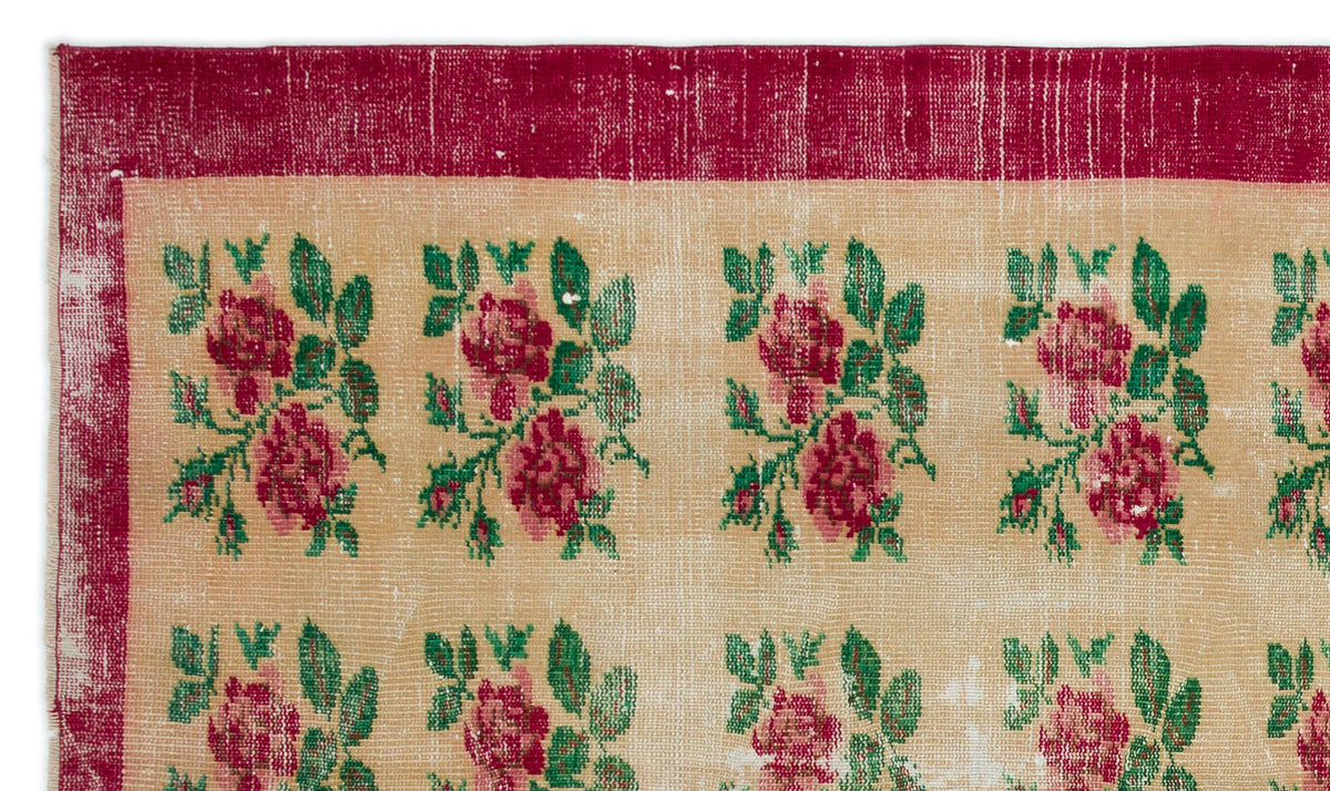 Beige rug with a repeating floral pattern in red and green, featuring a wide distressed red border.