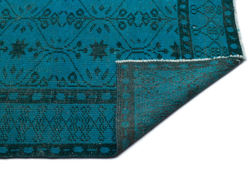 Load image 1 in gallery view. Teal and dark charcoal rug with a geometric diamond and floral pattern, shown with a corner folded over.
