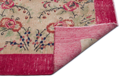 Load image 1 in gallery view. Beige rug with a distressed floral pattern in pink, green, and blue, featuring a wide magenta border and a folded corner.