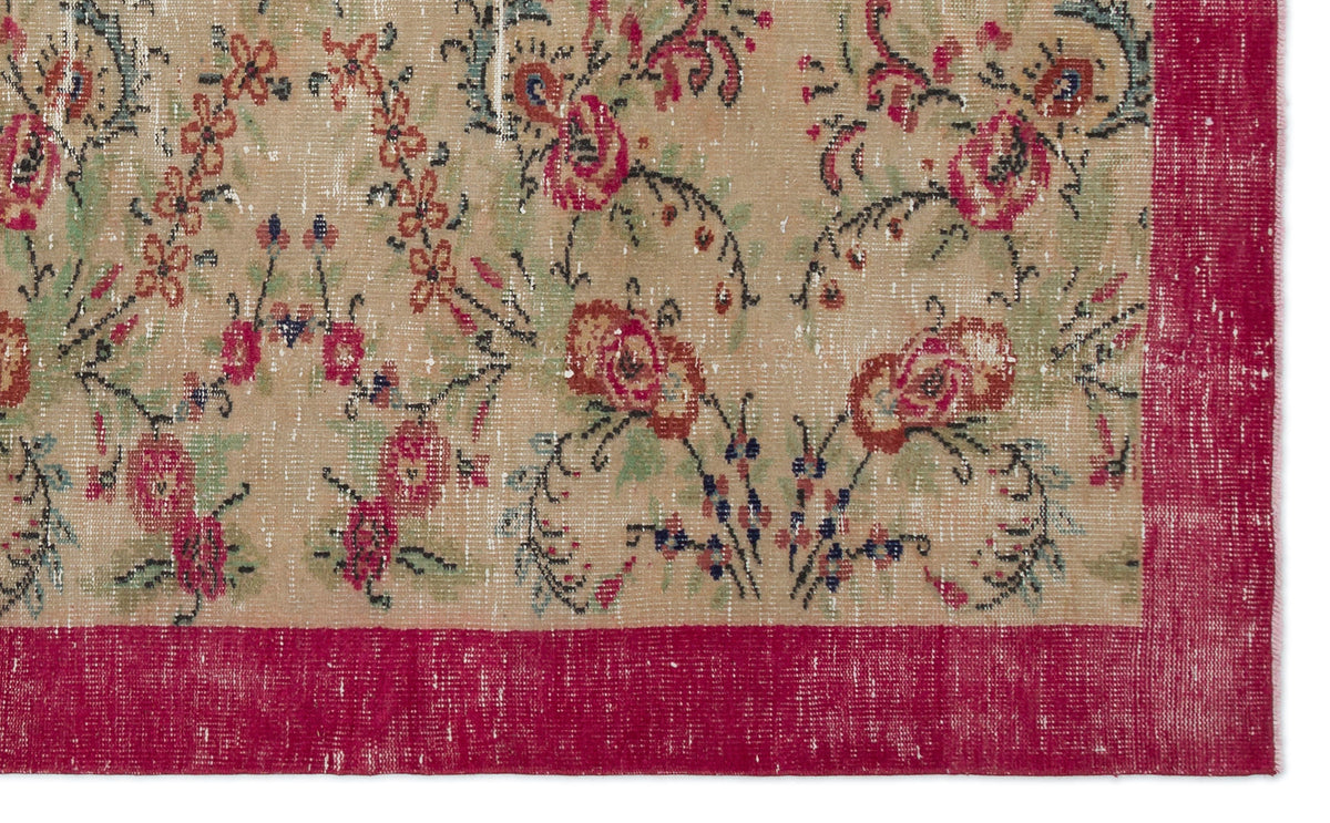 Distressed beige rug with a floral pattern in red, green, and black, featuring a wide, solid red border.