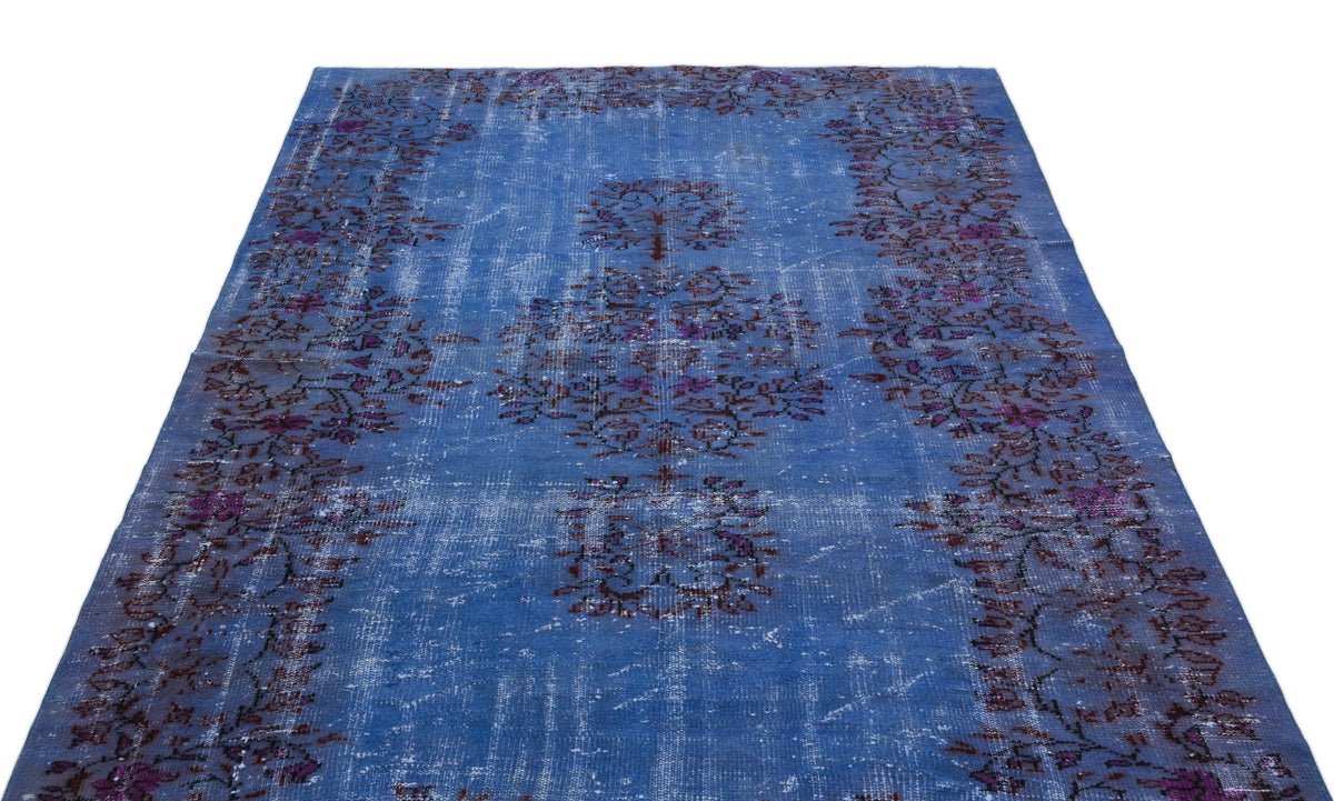 Distressed blue vintage-style rug with a central floral medallion and dark purple floral border on a white background.