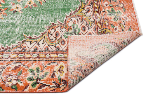 Load image 1 in gallery view. Green and orange vintage-style rug with a floral medallion pattern, shown with a corner folded over on a white background.