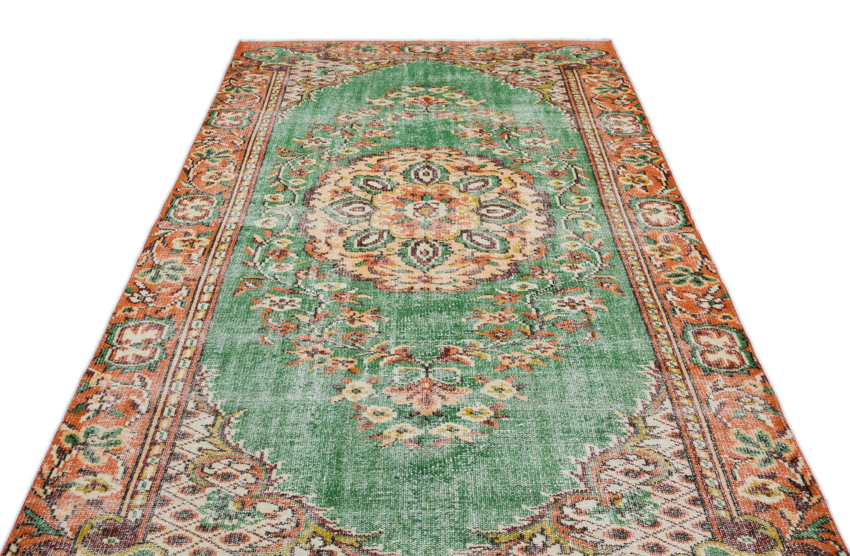 Green and orange vintage-style rug with a central floral medallion and ornate border pattern on a white background.