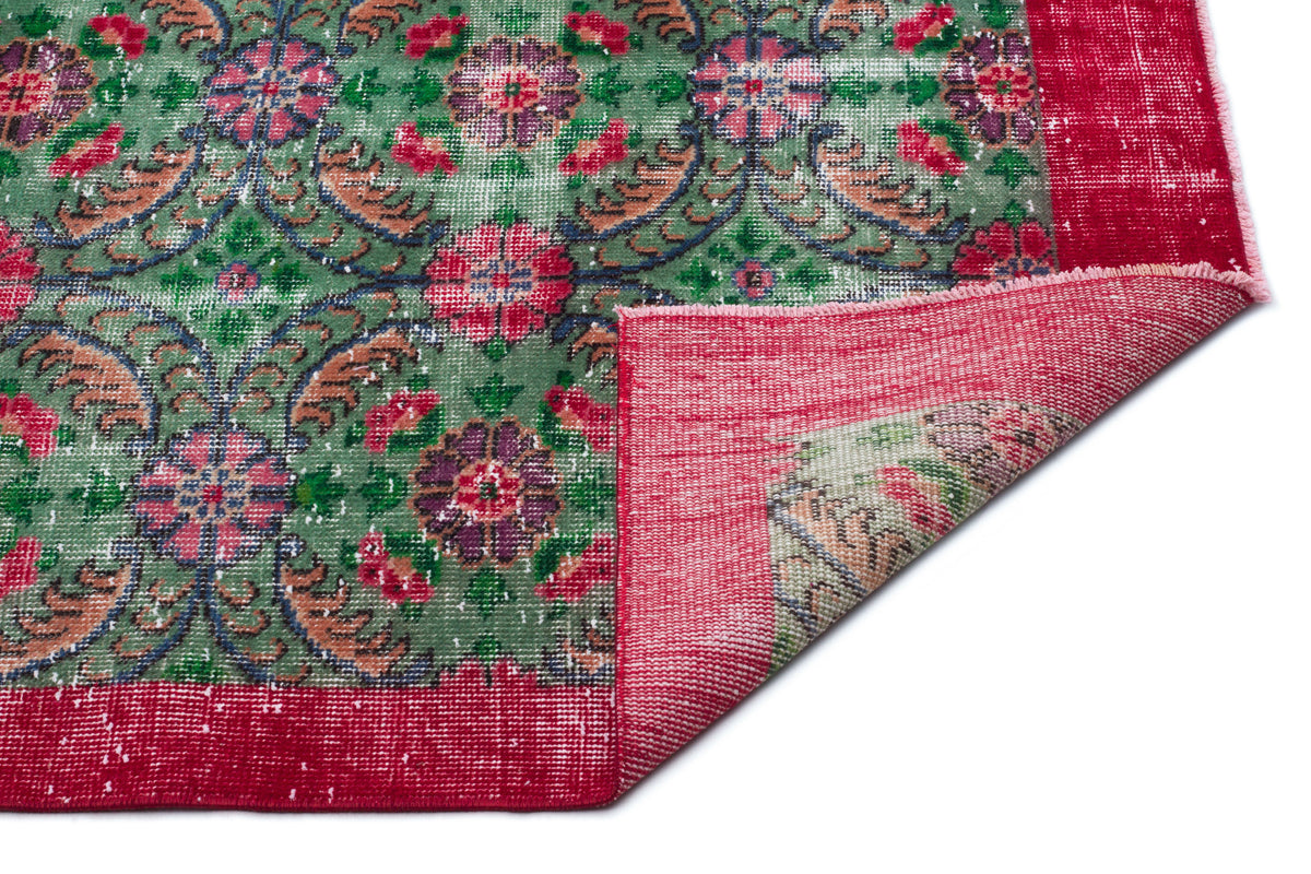 Green and red distressed rug with a floral medallion pattern and a folded corner showing the woven backing.