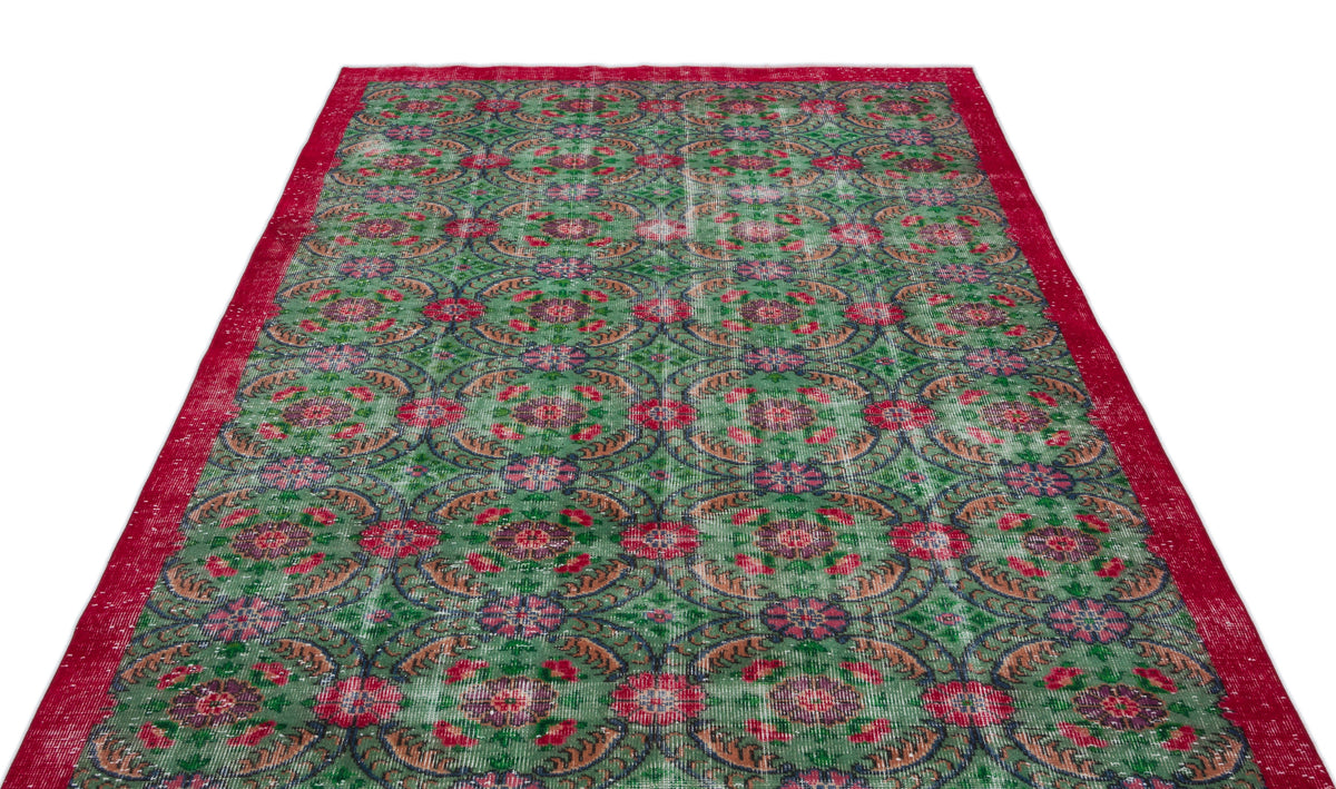 Distressed green rug with a repeating red and blue floral medallion pattern and a solid red border.