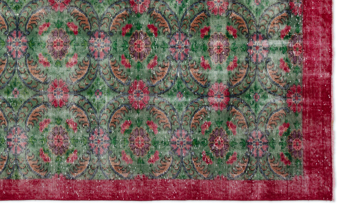 Distressed green rug with a repeating floral medallion pattern in red and tan, featuring a solid red border.