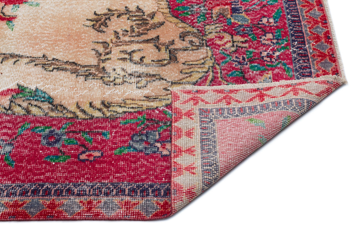 Distressed red and beige vintage-style rug with floral medallion patterns and a folded corner on a white background.