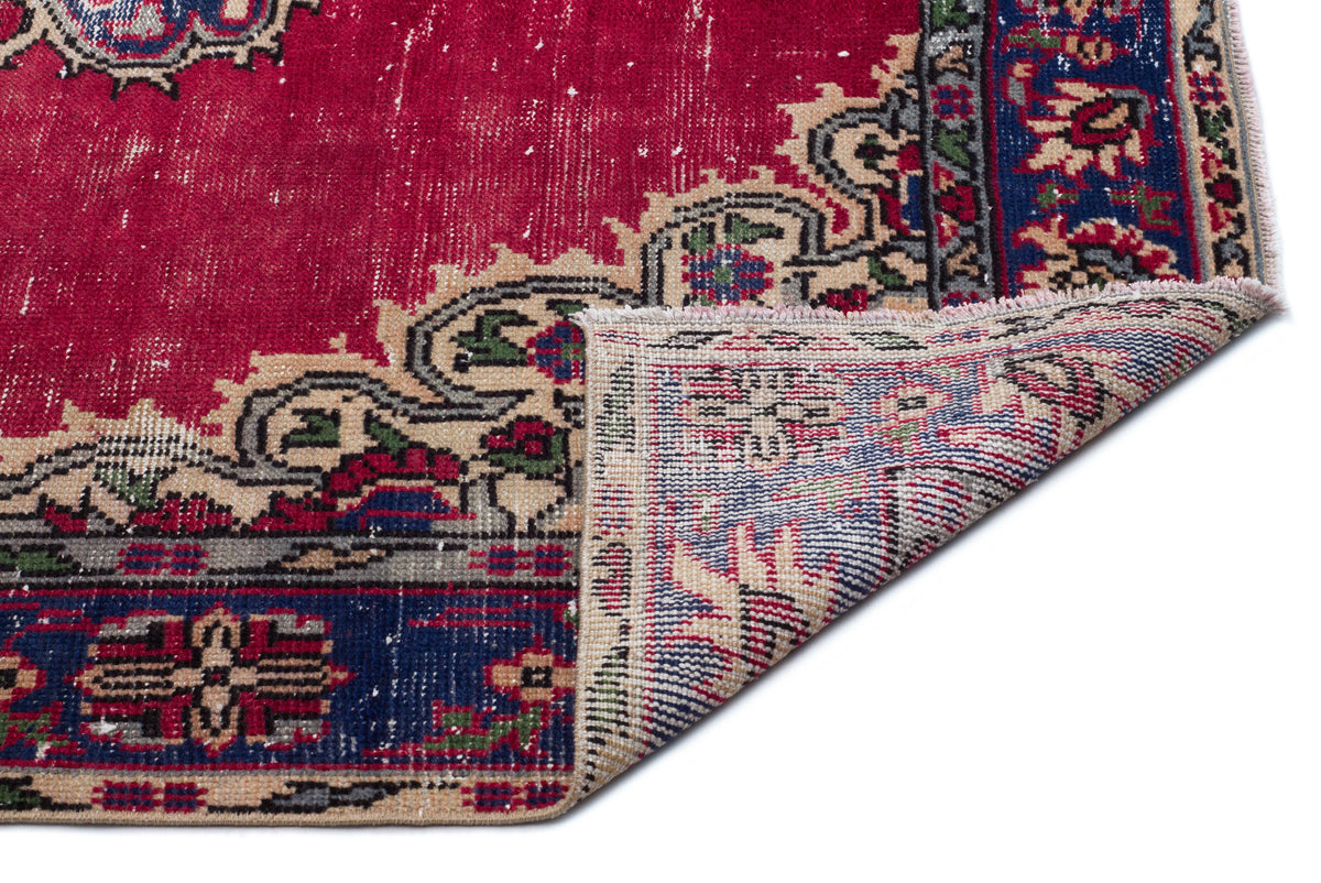 Distressed red, blue, and beige traditional rug with a floral medallion pattern, shown with a corner folded over.