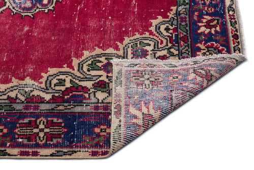 Load image 1 in gallery view. Distressed red, blue, and beige traditional rug with a floral medallion pattern, shown with a corner folded over.