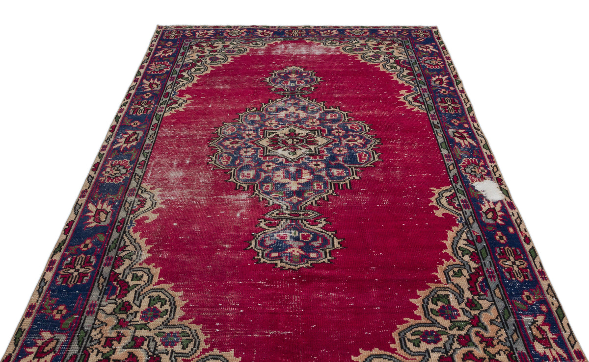Distressed magenta rug with a central blue and cream floral medallion and a decorative border on a white background.